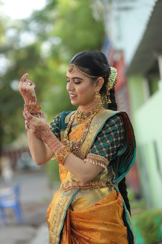 Bride in green and gold silk saree with mehendi and temple jewellery